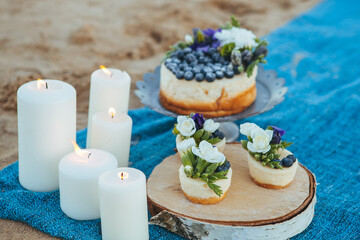 Obraz na płótnie Canvas Cheesecake and capcakes decorated by blueberries and flowers on the sand. Concept date,proposal, picnic. Natural food