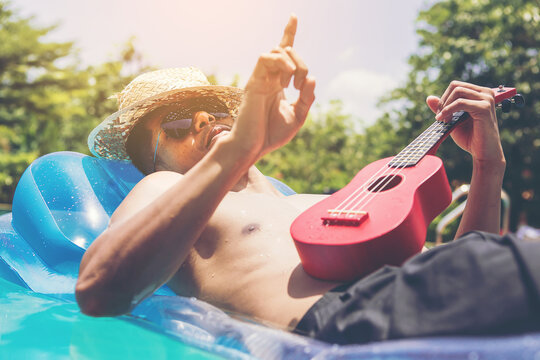 man with ukulele relaxing on the mattress beside the swimming pool. vacation and free time