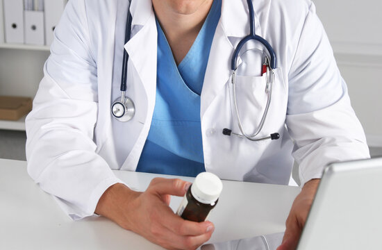 Male Doctor sitting at the table holding many different pills in his hand.