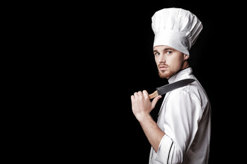 Young bearded man chef In white uniform holds  knife on  black background - Powered by Adobe