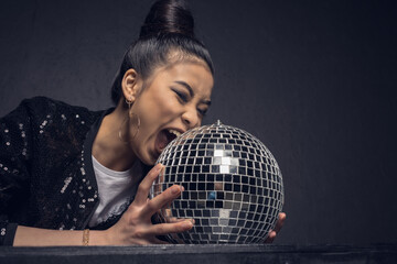 glamour asian girl biting disco ball isolated on grey