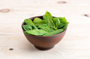 fresh green spinach leaves in ceramic bowl on wooden tabletop