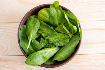 top view of green spinach leaves in ceramic bowl on wooden tabletop