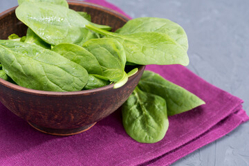 close up view of fresh spinach leaves in bowl on purple linen
