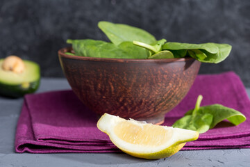 bowl of fresh spinach on linen with piece of lemon on tabletop