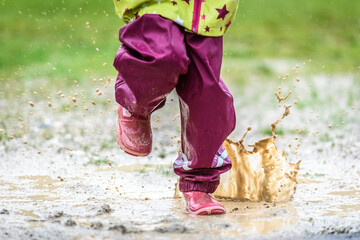 Children in rubber boots and rain clothes jumping in puddle.