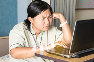 the asia woman in hospital room lying in bed sick and injured using internet in computer laptop feeling concern and serious about her job