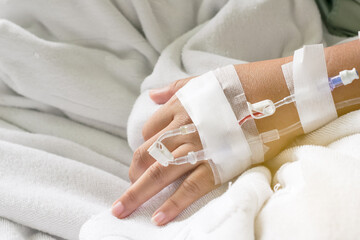 the Asian woman patient hand on IV drip with saline solution, fluid replacement therapy