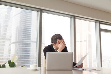 Sad entrepreneur sitting at office desk worries about bad financial results, head on hand. Fall in...