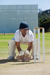 Portrait of wicketkeeper crouching behind stumps on field