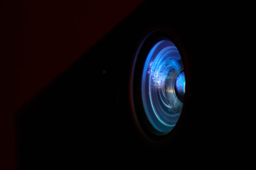 Photo depicts digital projector film presentation. Projector shiny colorful glass lens closeup, macro view, black background.
