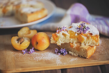Apricot pie with fresh apricots, decorated with lilac flowers on a wooden board.