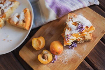 Apricot pie with fresh apricots, decorated with lilac flowers on a wooden board.