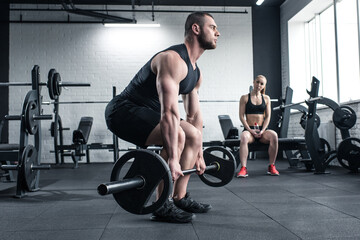 Fototapeta na wymiar man doing strength training with barbell while woman sitting at gym