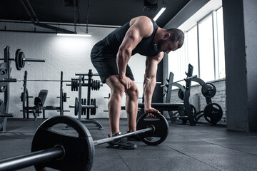 young adult exhausted bodybuilder holding barbell at gym