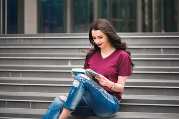 Beautiful woman reading a book on the steps of the building.