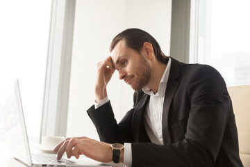 Obraz premium Young businessman at desk tired from routine laptop work. Entrepreneur boring at workplace, sick of monotonous work. Office worker procrastinates while trying complete dull report. Lack of motivation