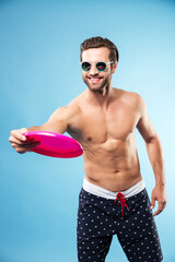 Young happy guy in summer shorts playing frisbee game