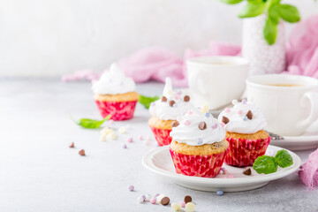 Mini cupcakes with white frosting cream and pink sprinkles on light gray background. Decorated with basil leaves. Party food concept. Copy space.