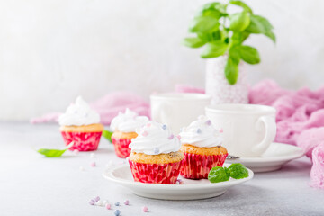 Mini cupcakes with white frosting cream and pink sprinkles on light gray background. Decorated with basil leaves. Party food concept. Copy space.