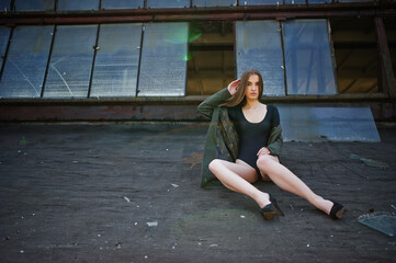 Sexy model girl wit long legs at black lingerie outfit body swimsuit combidress and jacket posed at the roof of abadoned industrial place with windows.