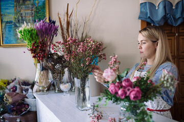 woman florist making bouquet of pink flowers indoor. Female florist preparing bouquet  in flower shop