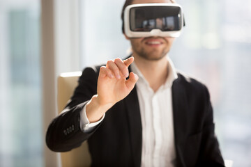 Entrepreneur in VR headset interacts with application virtual interface, pressing invisible buttons or selects menu items. Businessman works in office augmented reality. Cyberspace experience concept