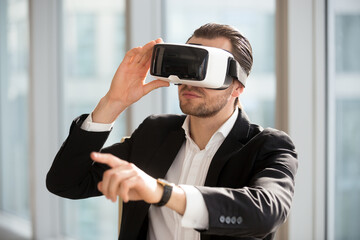 Businessman using technology of augmented reality in daily office work. Man ceo wearing virtual reality glasses, pointing at the air. Office worker in electronics 3d goggles interacts with simulation