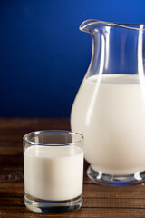 Close-up view of fresh organic milk in glass jug and glass on wooden table top