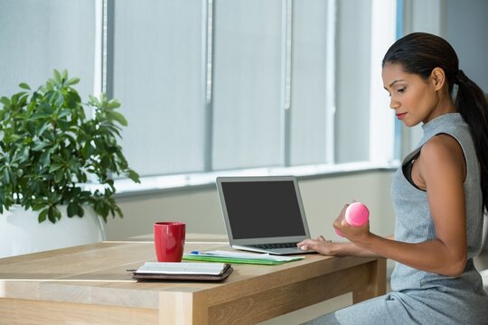 Executive exercising with dumbbells while using laptop