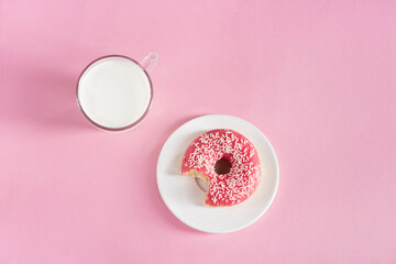 top view of glass cup of milk with donut on plate on pink background