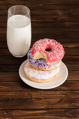 close up of glass of milk with donuts on plate on wooden background