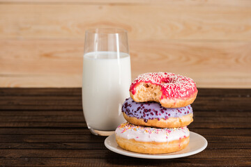 close up of glass of milk with donuts on plate on wooden background