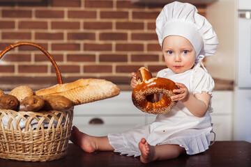 Funny little cook in kitchen with bakery. Scullion eating a bagel