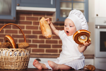 Funny little cook in kitchen with bakery. Basket with loafs a bread and bagels