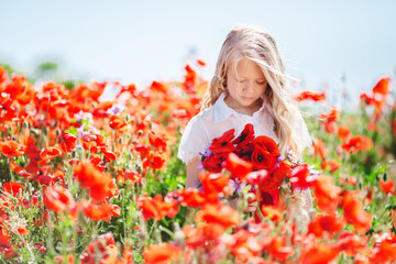 Naklejka premium Sad child girl with bouquet of red poppies and purple flowers