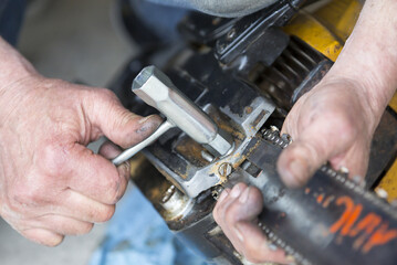 Caucasian man is fixing a chain saw. Dirty hands from oil and dust.