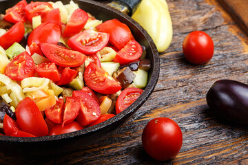 Sliced fresh vegetables in pan with spices and ingredients on wooden table