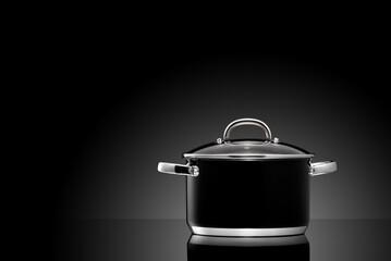 Black kitchen pot on glass surface and dark background