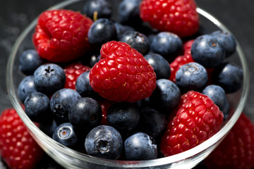 fresh berries in a glass bowl on dark background, closeup
