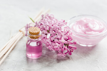 Fototapeta na wymiar lilac cosmetics with flowers and spa set on stone table background