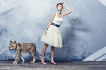 Beautiful fashionable young woman with a little alive lion cub