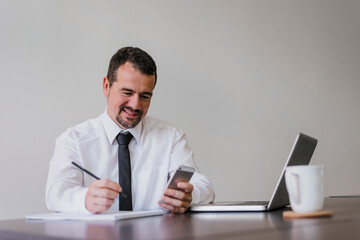 Positive senior menager holding smartphone and writing notes.