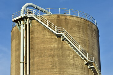 Concrete cylindrical industrial silo with metal stairs with safety railing and large bore pipes.