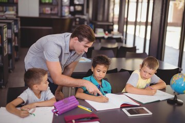 Teacher helping schoolkids with their homework in library
