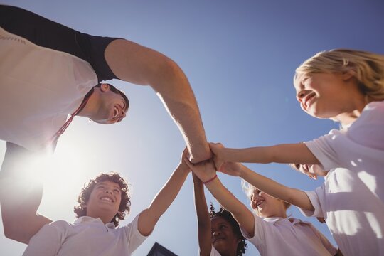 Happy coach and schoolkids forming handstack