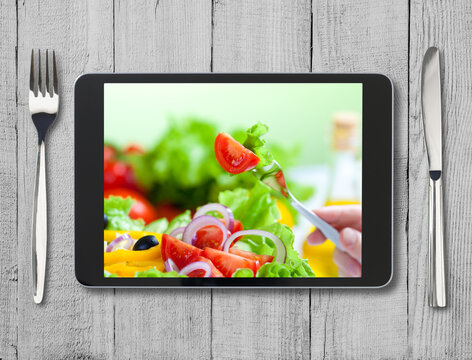 black tablet pc with healthy food on screen and wooden table