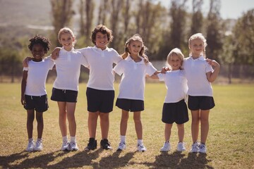 Obraz premium Portrait of happy schoolgirls standing with arms around in park