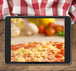 black tablet pc with pizza displayed on wooden table and picnic tablecloth