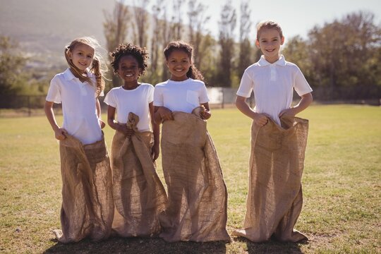 Portrait of happy schoolgirls standing in sack during race
